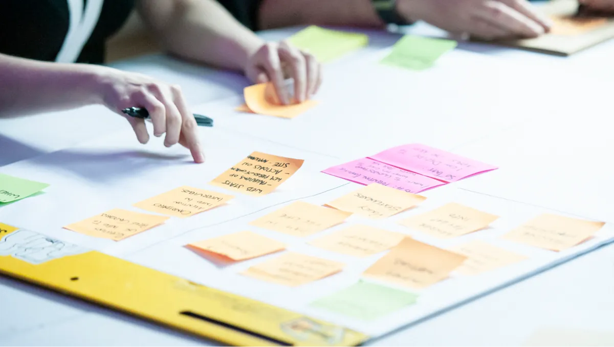 A close-up of people arranging sticky notes on a flip chart pad.