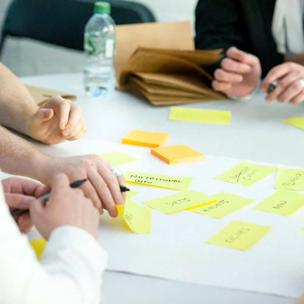 A close up of a group of people adding sticky notes to a sheet of paper during a user experience exercise.