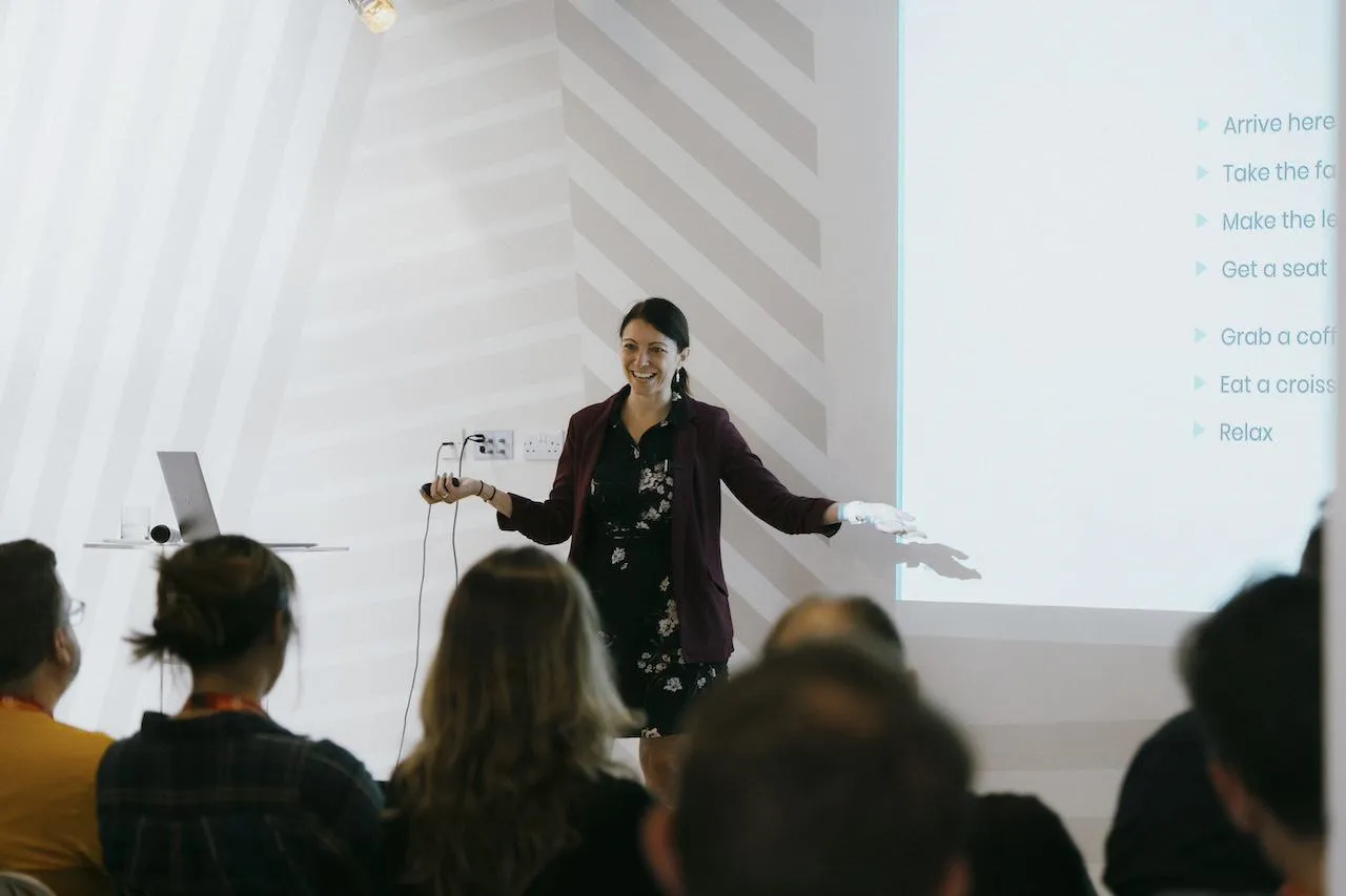 A woman smiling at a crowd as she does a presentation