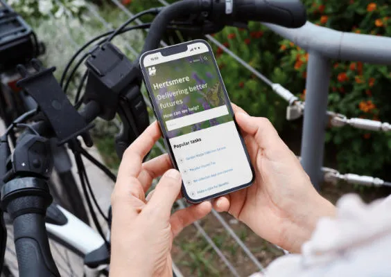 A closeup of a person's hands as they use the Hertsmere Borough Council website on a mobile phone.