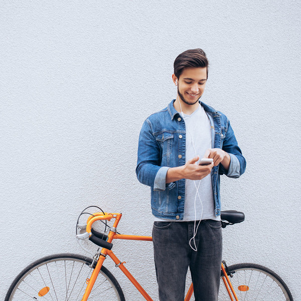A young man standing next to an orange bicycle and using his mobile phone.
