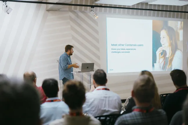A male presenting to a crowd using a laptop and projector screen.