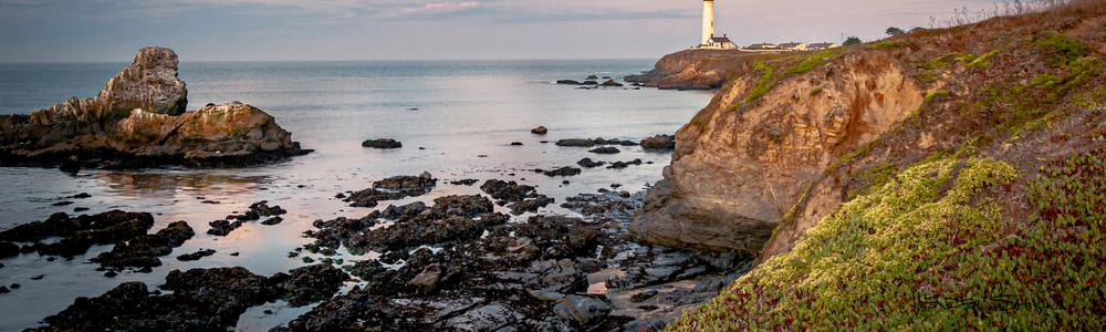A wide banner taken from the bottom of the coastal landscape, showing the rocky shoreline and water